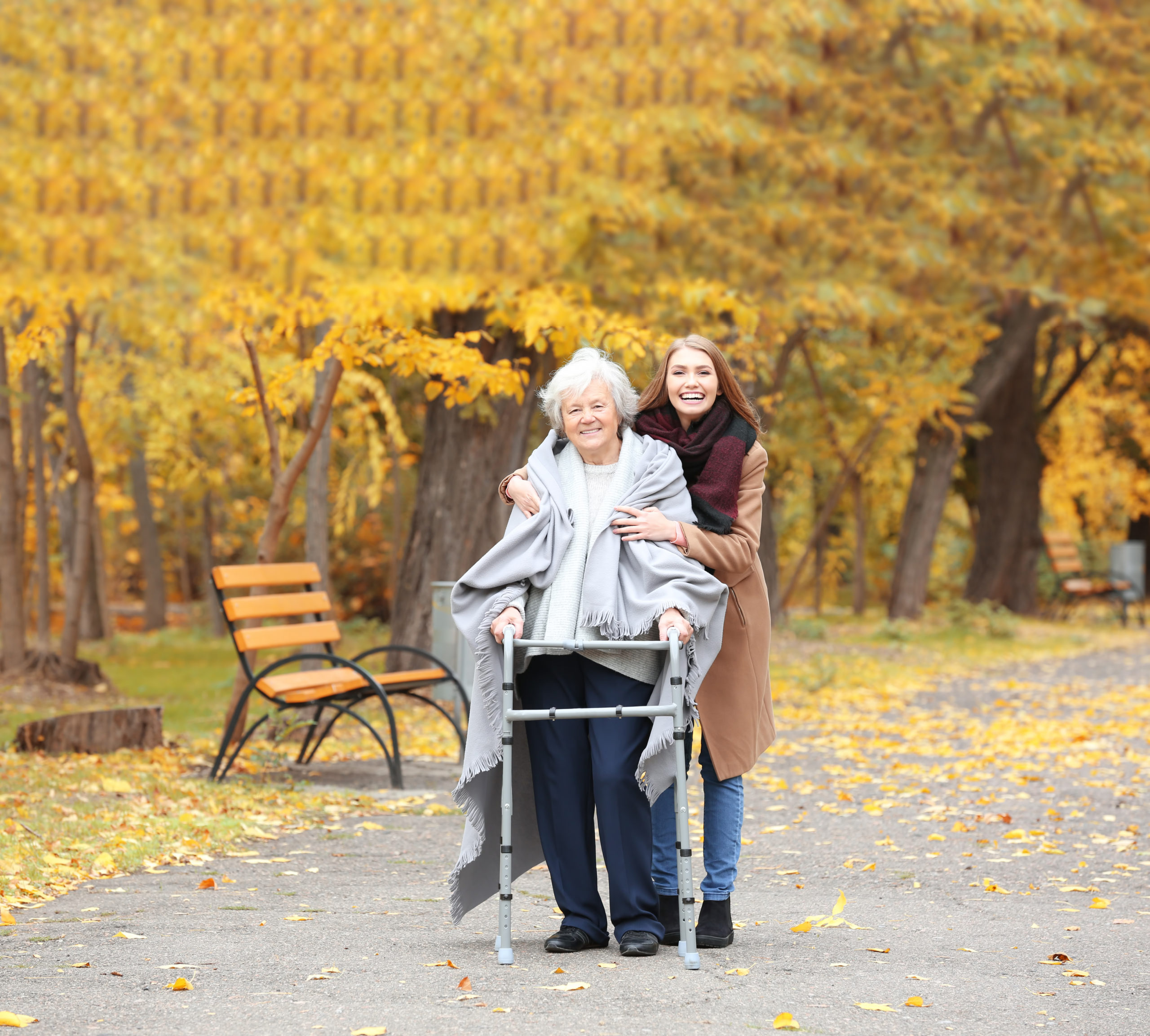 Senior woman with walking frame and young caregiver in park